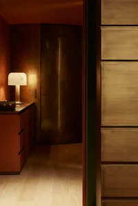 A modern kitchen with wood cabinets, featuring a table lamp with a white shade casting a warm glow on the wooden surfaces.