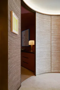 A view into a modern office studio with textured wall coverings and a softly illuminated table lamp.