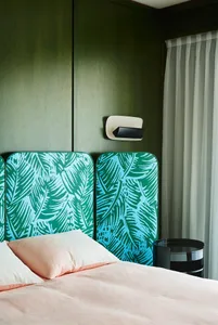 A modern bedroom featuring a bed with pink bedding, a green palm leaf print headboard, and a window with sheer curtains.