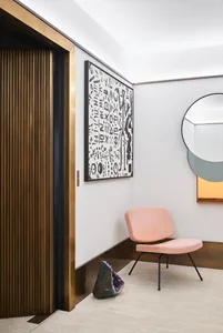Lobby featuring modern brass and wooden furniture, with a pink upholstered chair and an abstract wall art.