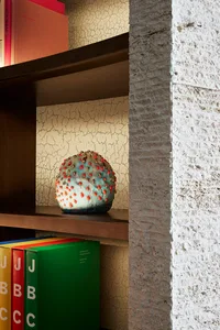 A ceramic object with red and gold accents sits on a wooden shelf in an urban industrial interior design setting.