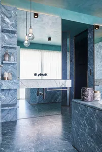 Modern bathroom interior with marble tiles, a floating vanity sink with black faucets, and a large mirror.