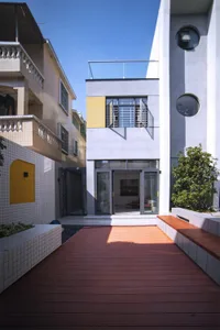 A modern, concrete exterior of a home with a wooden walkway and surrounding greenery.