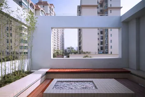 A modern, urban balcony featuring concrete walls, wooden flooring, stone planter, and white cushioned seating.