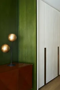 Modern interior featuring green walls, white cabinets, brass lighting, and wooden floors.