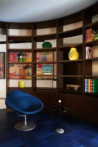 A modern home office featuring a curved wooden bookshelf filled with colorful objects and books.