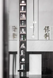 A modern living room featuring sleek marble decor, with a bookshelf filled with books and decorative items, and a hanging lig