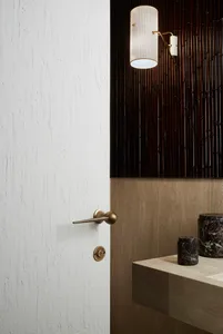 A modern minimalist bathroom featuring a white-painted wooden door with a sleek brass handle and a contemporary light fixture