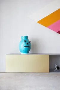 A modern ceramic vase with a face design on a clean, minimalist cabinet in a contemporary interior setting.