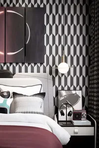 A modern bedroom featuring a geometric patterned backdrop, a bed with a white headboard and burgundy accents, and a hanging l
