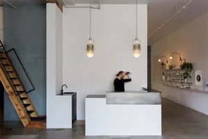 A minimalist coffee shop with a modern metal counter, white walls, and pendant lights hanging from the ceiling.