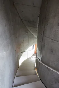 A modern staircase with white steps and concrete walls and ceiling.