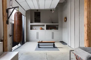 Modern industrial-style home gym with a concrete floor, plywood cabinets, and metallic accents.
