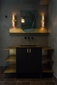 A modern minimalist bathroom featuring a brass cabinet with an integrated sink, accompanied by minimalist sconces and a textu