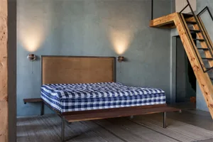 A minimalist bedroom with a wooden bed frame, checkered bedspread, and a leather headboard.