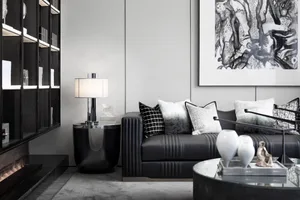 A modern living room featuring a black leather sofa adorned with multiple pillows, a glass coffee table, and a bookshelf fill