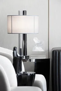 Modern lounge space featuring a glass and chrome table lamp with a white shade, accompanied by a transparent plastic sculptur
