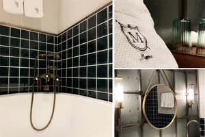 Modern bathroom with black ceramic tiles, a white bathtub, and a towel rack with a branded towel.