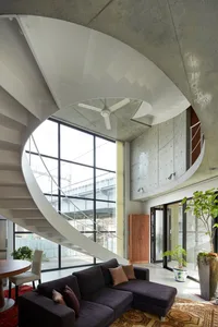 Modern residential living room with a spiral concrete staircase, large windows, and a dark sofa.