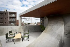 Outdoor concrete rooftop with wooden table, chairs, and greenery