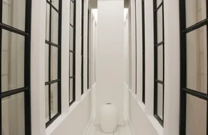 A minimalist hallway with white walls and windows, featuring a single white vase.