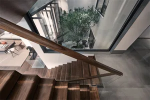 Modern architectural design featuring wooden stairs with glass railing and a central courtyard with a tree and sculpture.