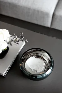 A sleek, modern coffee table adorned with a mirrored bowl and a vase of white roses, alongside a book.