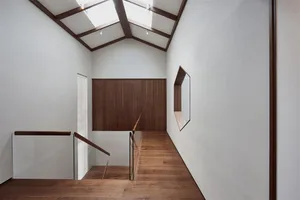 Modern interior design featuring a wooden stairwell with a glass railing and a skylight ceiling.