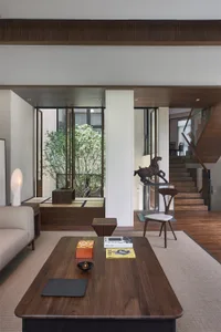 A modern living room with wooden furniture, featuring a large window, a coffee table with books and a bowl, and a wooden floo