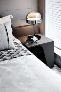 A minimalistic bedroom featuring a metallic table lamp on a sleek, modern nightstand.