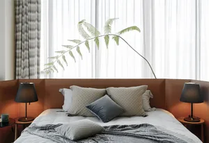 A minimalist bedroom with a bed adorned with multiple pillows, a blanket, and side tables with lamps and a plant.