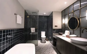 Modern bathroom featuring black tiles in a geometric pattern, with a freestanding bathtub, a toilet, a vanity with a white si