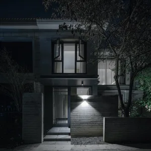 A modern house facade made of concrete with lights illuminating the entrance.