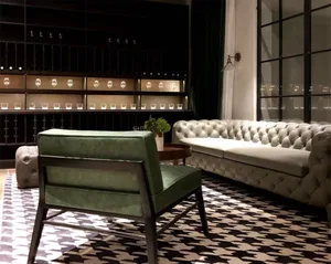 A modern living room with a green armchair, white tufted sofa, and black and white patterned rug.