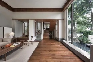 A modern minimalist living room with wooden flooring and white walls, featuring a sofa, coffee table, bookshelf, and a view o