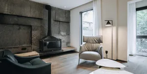 A modern living room features a concrete and stone fireplace, wooden flooring, leather and marble furniture.
