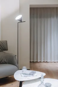 A modern living room featuring a grey leather sofa, a triangular marble coffee table, and a black floor lamp with a white sha