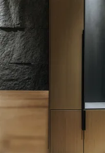 A minimalist residential kitchen featuring wooden cabinets and a stone wall.