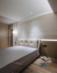 Bedroom with minimalist design, white bed, and wooden floor and headboard.