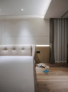 A minimalist bedroom with white wooden flooring, white headboard, and a few scattered books.
