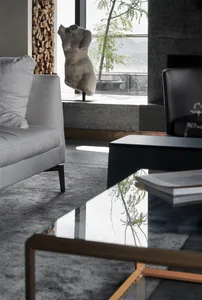 A modern minimalist living room featuring a glass coffee table and a sleek black leather chair.