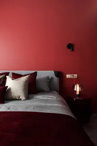 A minimalist bedroom with a maroon and gray color scheme, featuring a bed with a textured pillow and a wall-mounted light fix