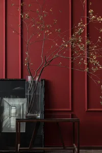 A vase containing branches with dried leaves on a wooden side table in a red-walled room.