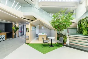 A modern workspace interior with green artificial grass, wooden furniture, and concrete elements.
