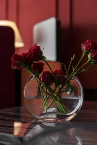 A transparent glass vase containing several red roses on a reflective surface.