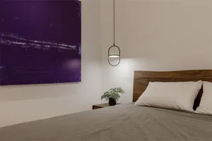 A minimalist bedroom with a wooden headboard and a purple abstract painting on the wall.
