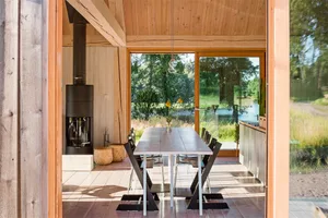 A minimalist dining room with a wooden table and chairs, large windows overlooking a natural landscape.