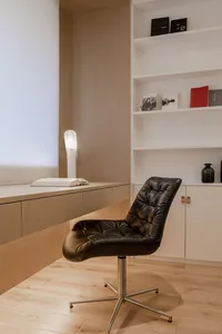A minimalist home office with a wooden desk, leather chair, and shelves.