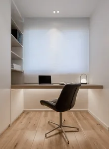 A minimalist office space featuring a desk with a laptop, a black chair, and a bookshelf.