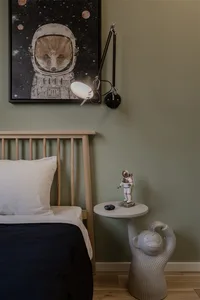 A modern bedroom featuring a wooden bed frame with a white pillow and a black blanket, a wall-mounted lamp, and a small table